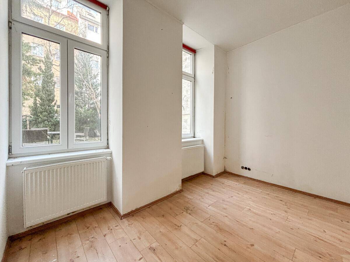 Helles Zimmer mit Dielenboden und Blick auf den grünen Innenhof, ideal für Ruhe.
