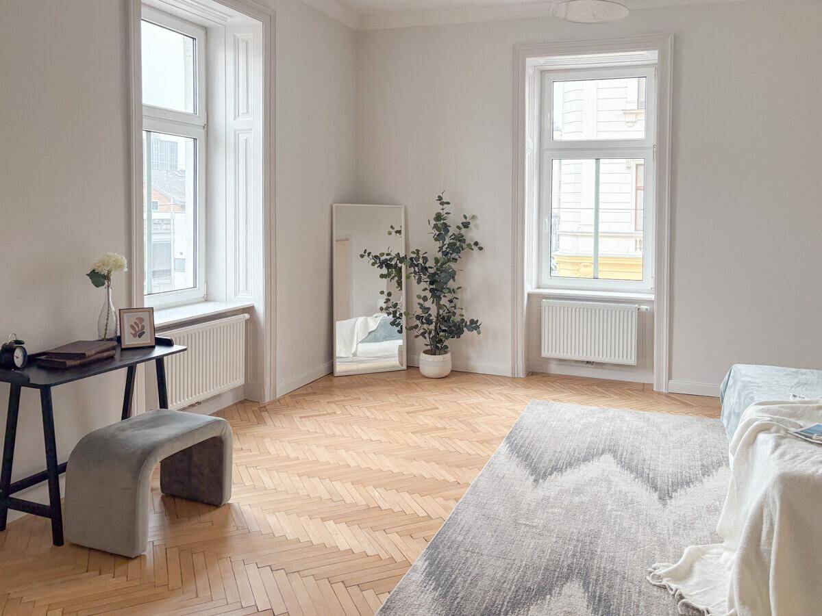 Geräumiges Schlafzimmer mit Fischgrätparkett, hohen Fenstern und viel Tageslicht.