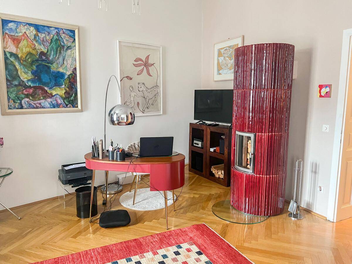 Gemütliches Wohnzimmer mit modernem Kachelofen, Schreibtisch und farbenfroher Kunst.