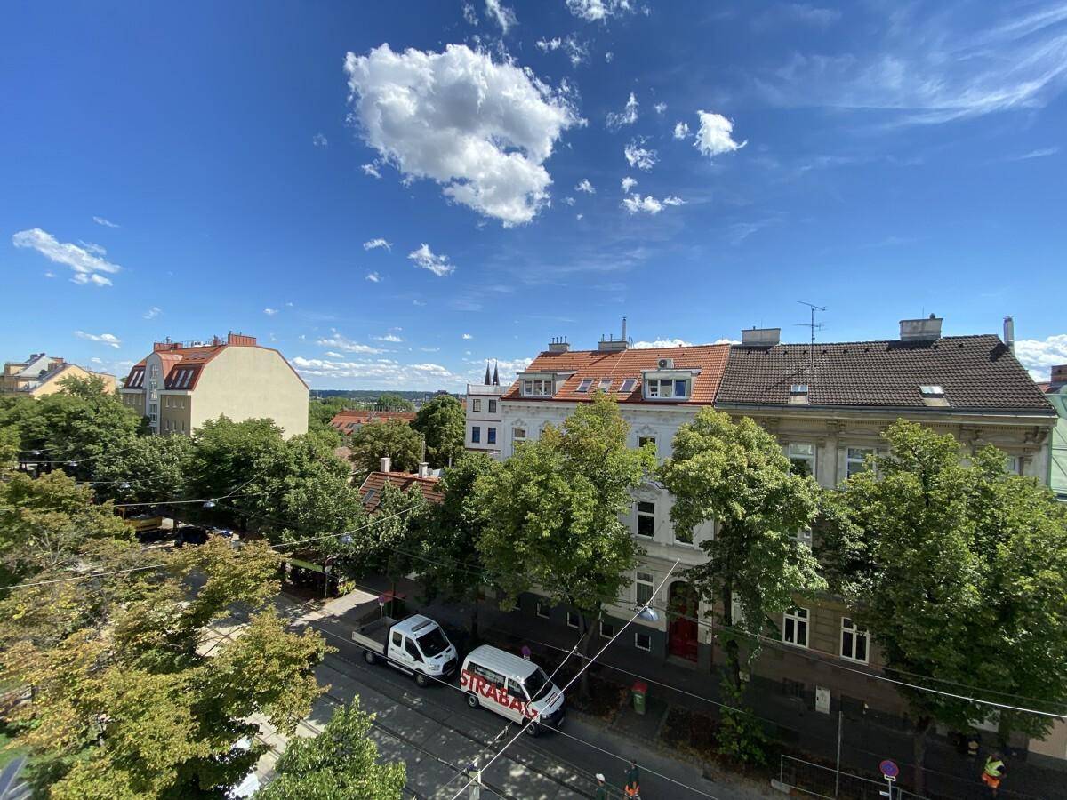 Panoramablick über eine städtische Straße mit Gebäuden und üppigem Grün unter klarem Himmel.