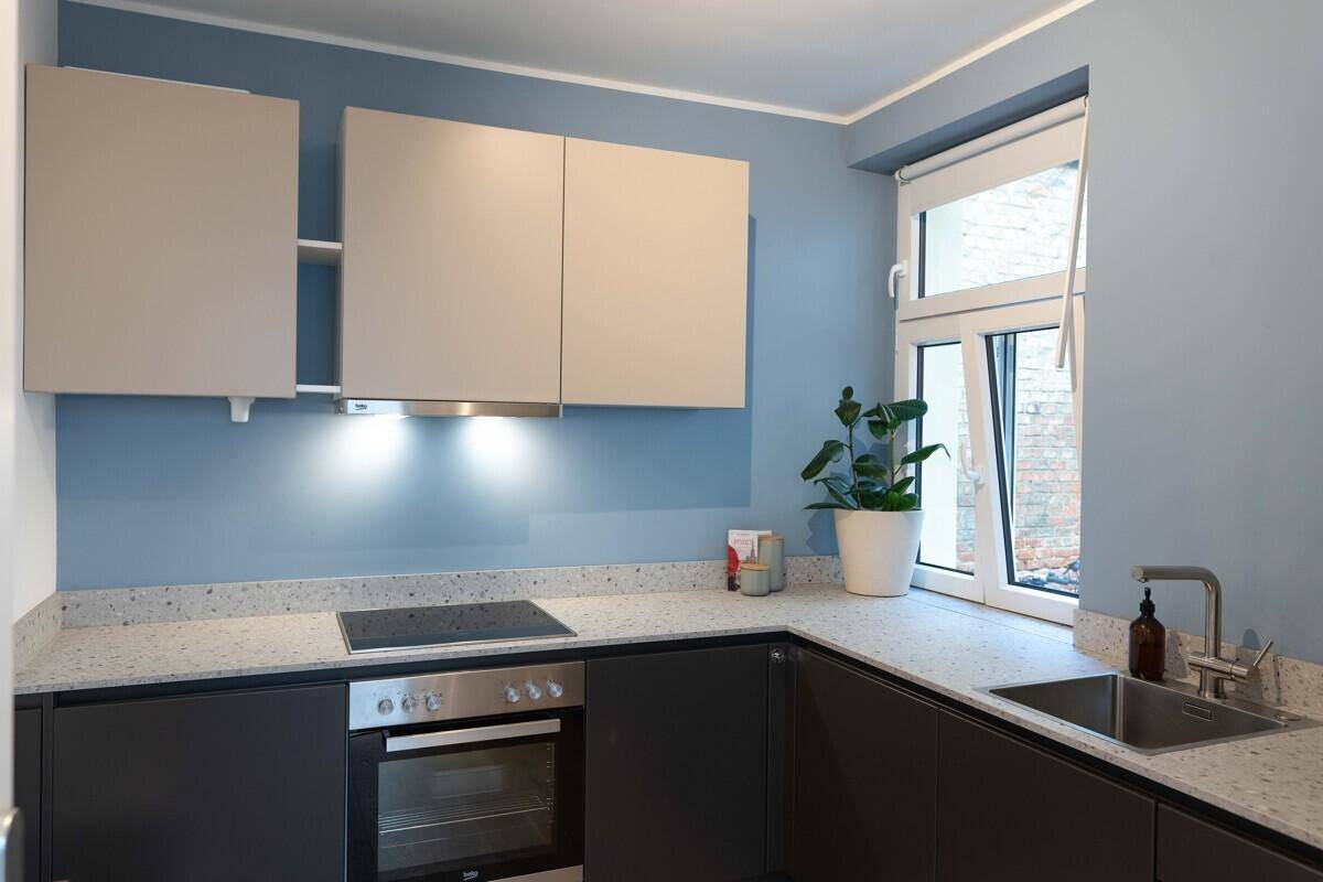 Moderne Küche mit blauen Wänden, hellen Schränken und Induktionskochfeld.