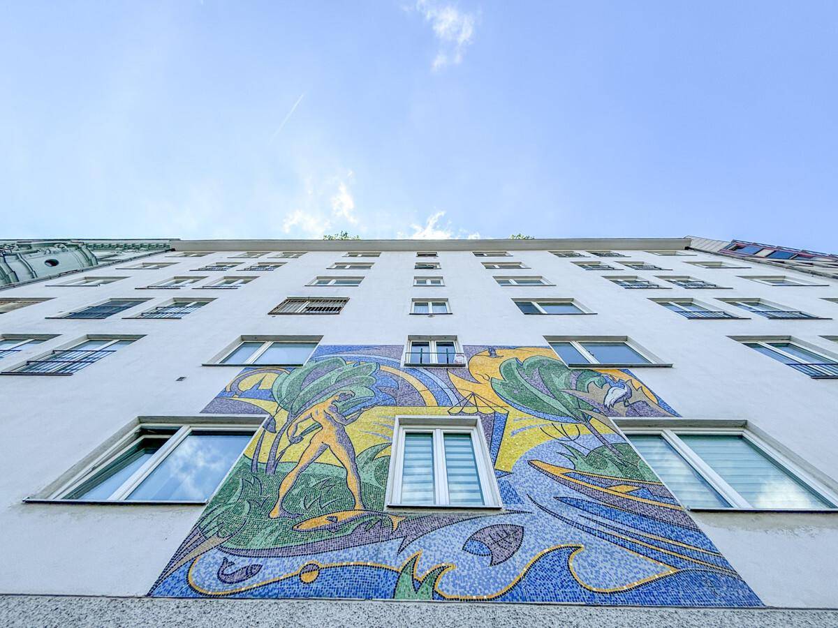 Fassade eines Gebäudes mit farbenfrohem Mosaik und vielen Fenstern unter blauem Himmel.