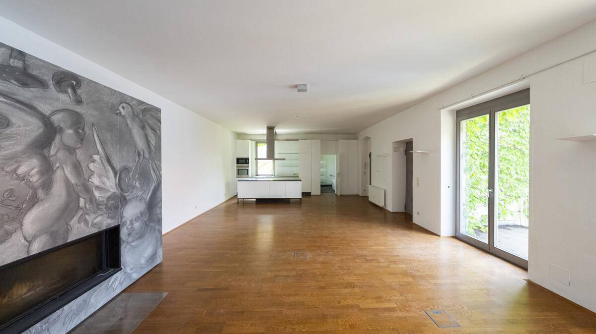 Heller offener Wohnbereich mit Holzboden, Kamin und Blick auf die angrenzende Küchenzeile.