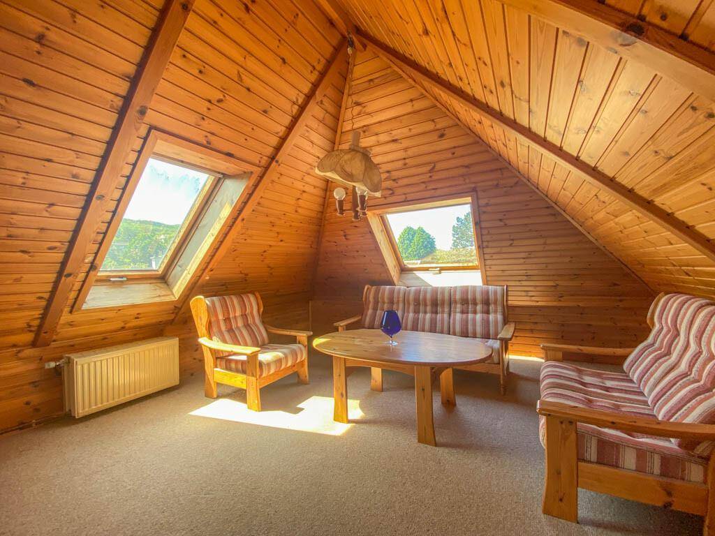 Gemütlicher Dachboden-Wohnbereich mit Holzverkleidung, Dachfenstern und rustikalen Möbeln.