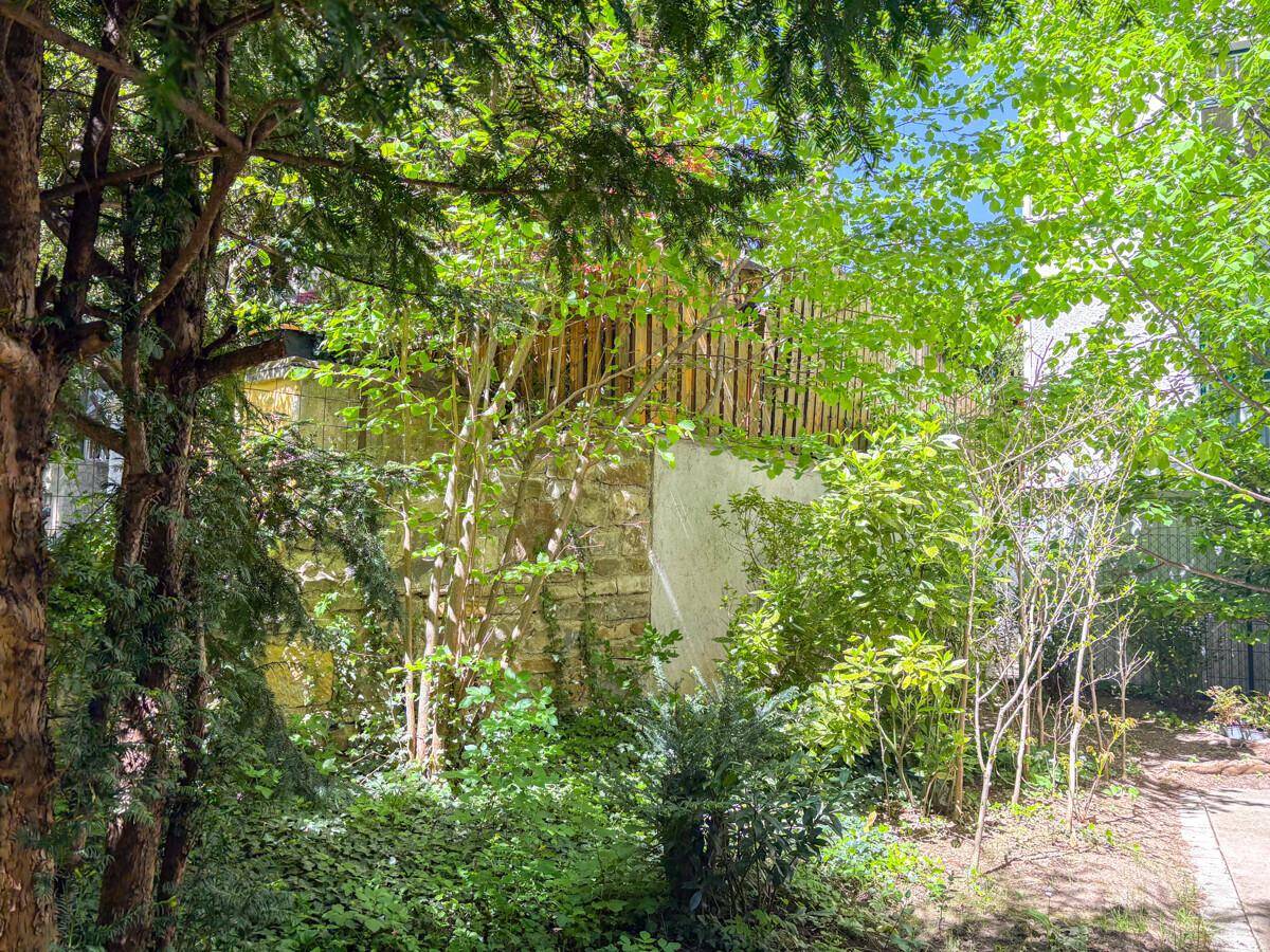 Dichter, grüner Garten mit Bäumen, Sträuchern und einer Steinmauer im Hintergrund, die Privatsphäre bietet.