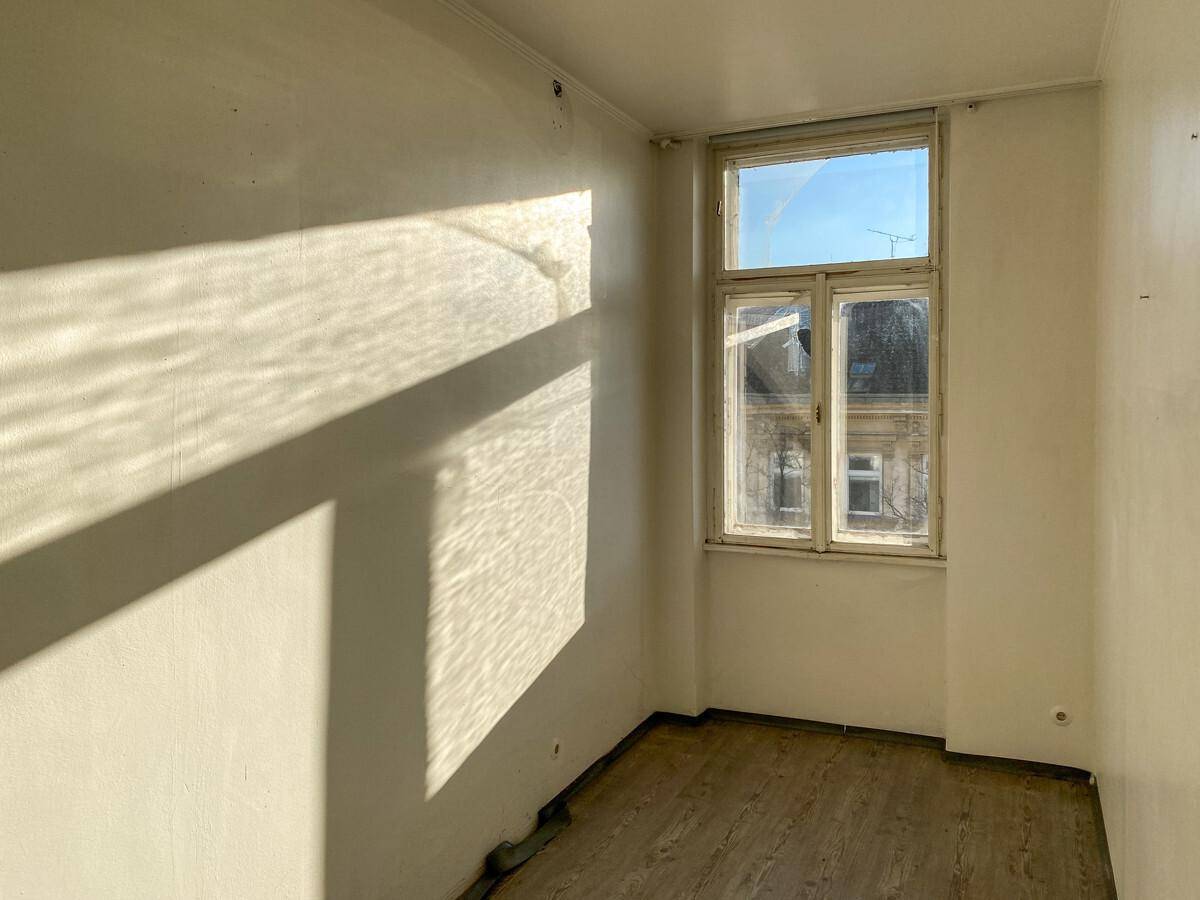 Leeres Zimmer mit einem Fenster, das viel Sonnenlicht hereinlässt und Schatten wirft.