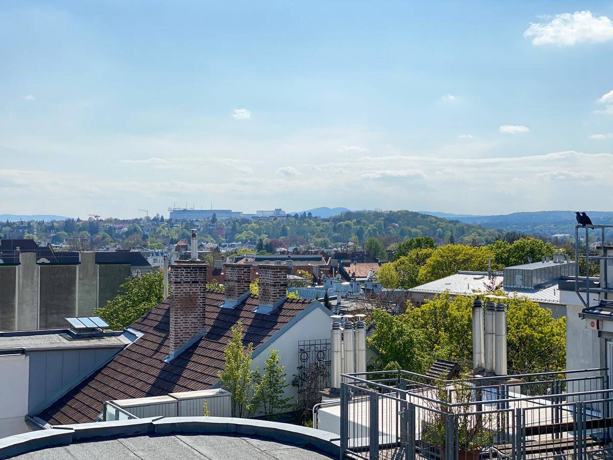 Panoramablick über die Dächer der Stadt mit grünen Hügeln und einem weiten Horizont.