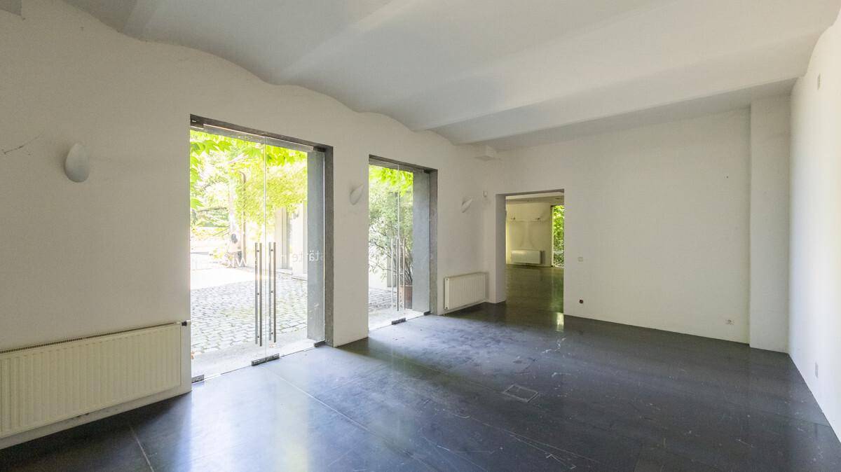 Heller Innenraum mit dunklem Boden und großen Glastüren, die viel Tageslicht hereinlassen und den Blick nach draußen freigeben.