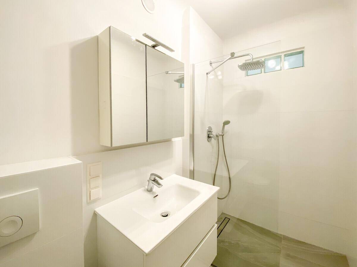 Modernes Badezimmer mit weißer Einrichtung, begehbarer Dusche und Spiegelschrank über dem Waschbecken.