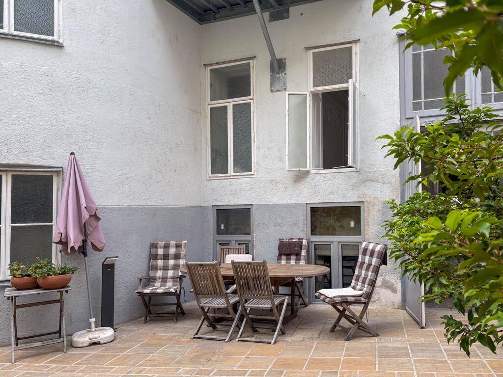 Gemütlicher Innenhof mit Sitzgelegenheiten, Sonnenschirm und Pflanzen in städtischer Umgebung.