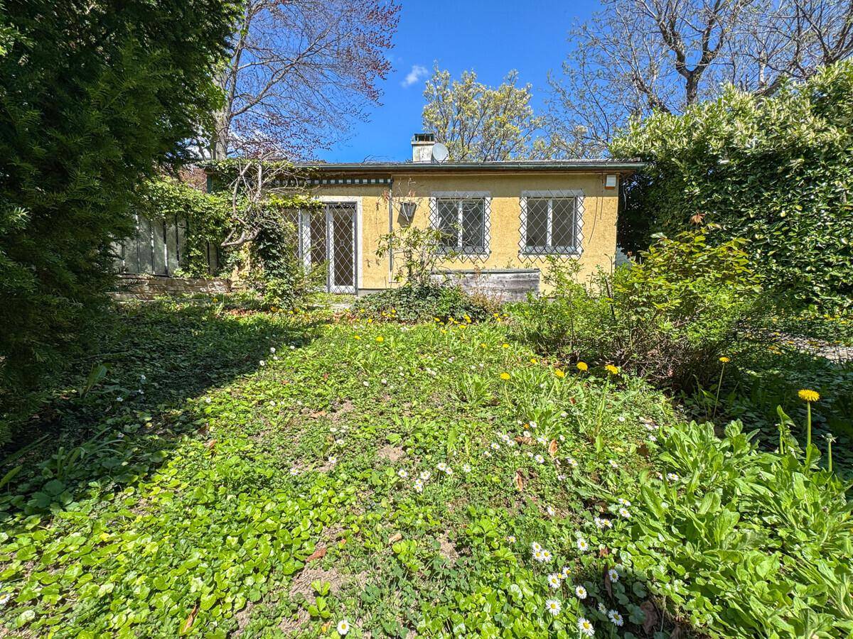 Rückansicht des gelben Hauses vom Garten aus, umgeben von üppigem Grün und Bäumen.