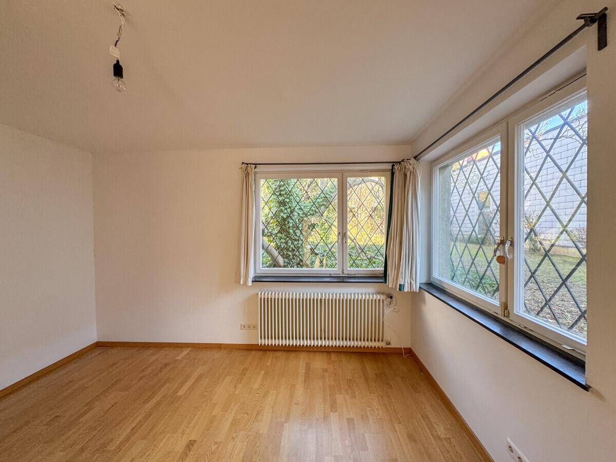 Helles Zimmer mit Holzboden, großen Fenstern und Blick ins Grüne.