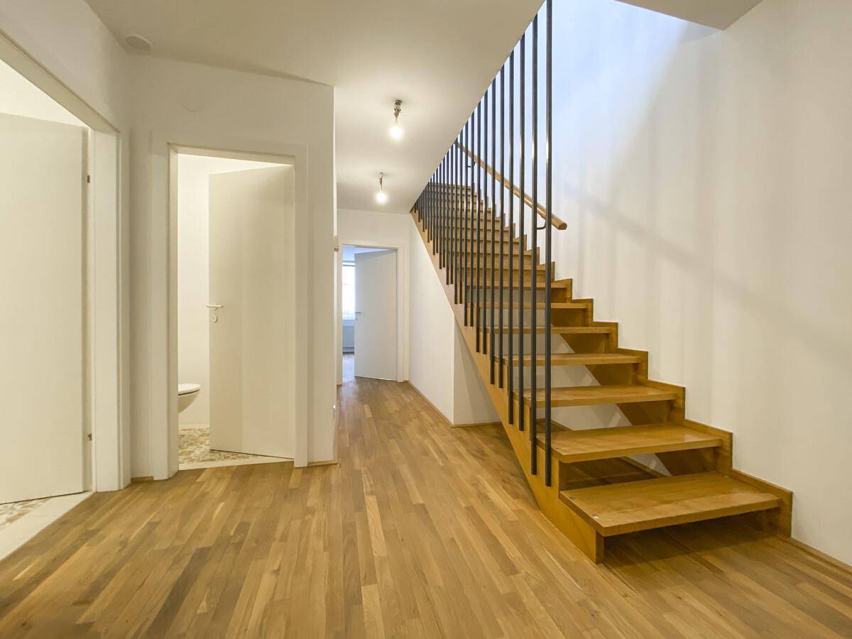 Heller Flur mit Holztreppe und Parkettboden, der zu weiteren Räumen führt.