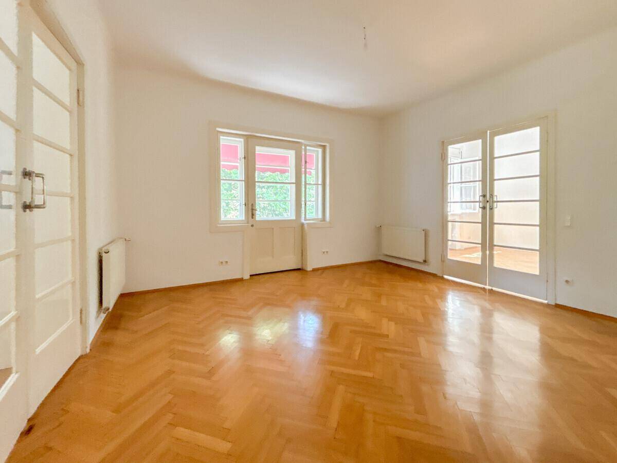 Helles Zimmer mit Fischgrätparkett und Zugang zu einem Balkon oder einer Terrasse.