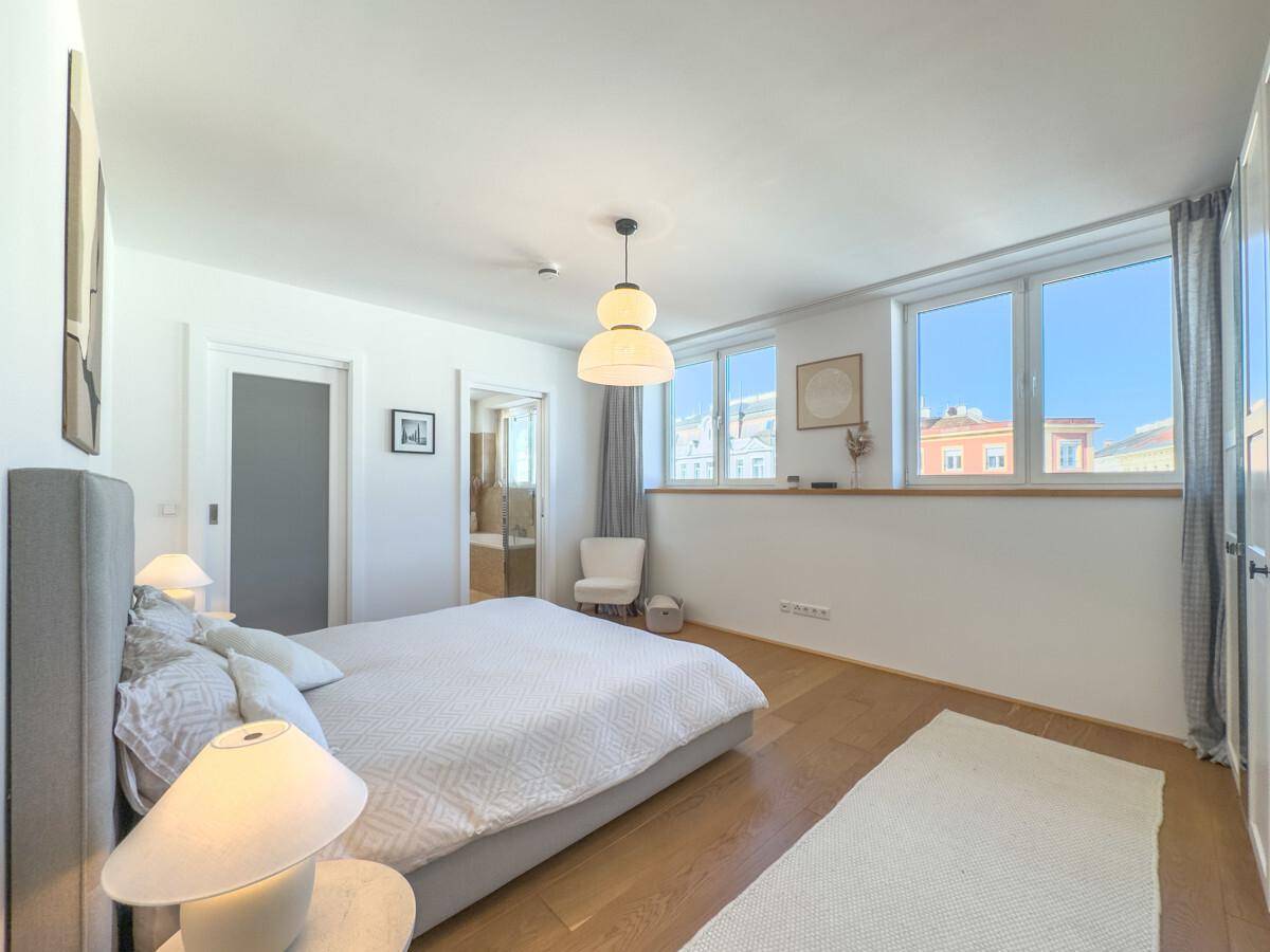 Modernes Schlafzimmer mit Holzboden, großen Fenstern und direktem Zugang zum Badezimmer.