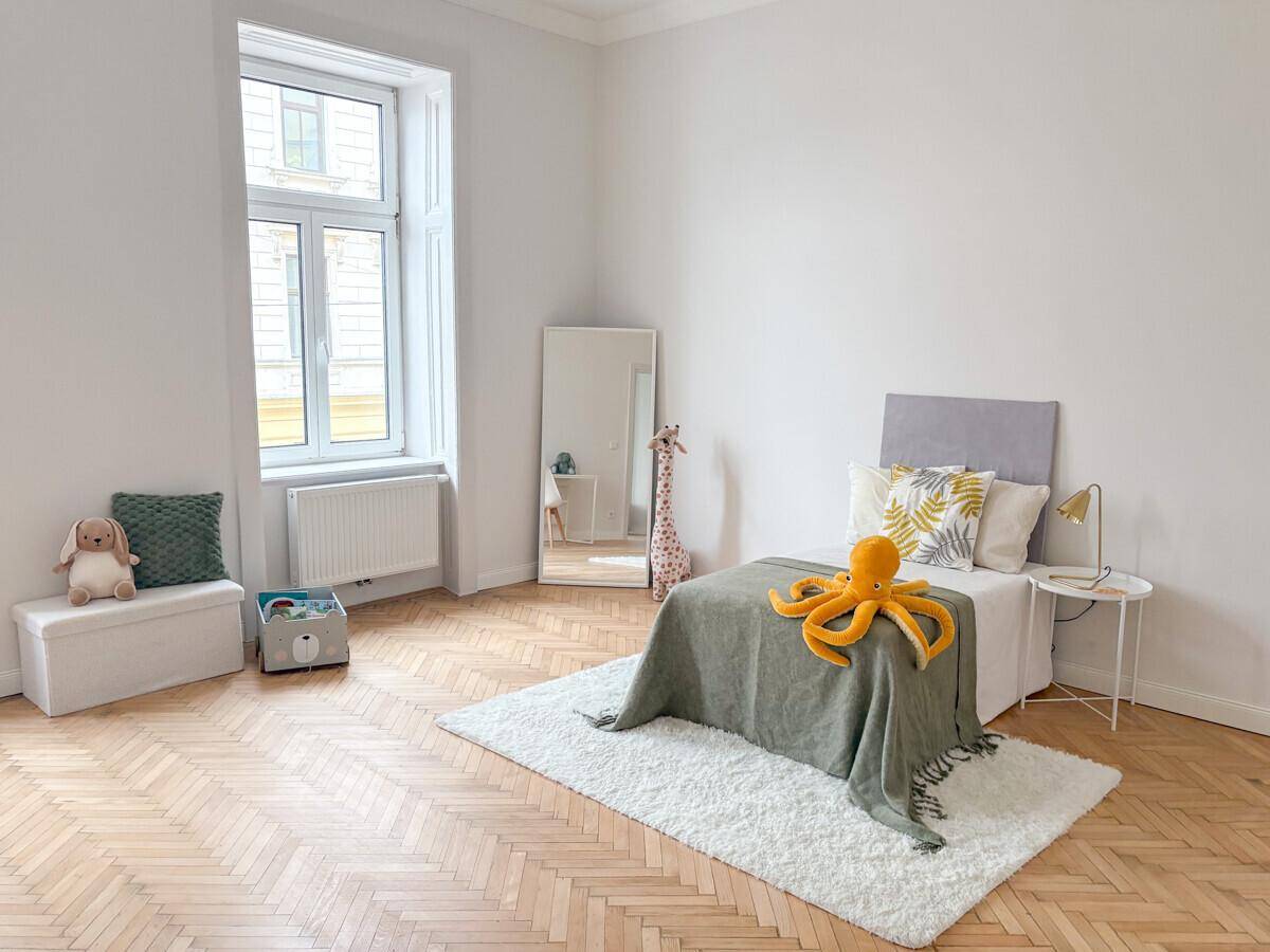 Helles Kinderzimmer mit Fischgrätparkett, Einzelbett und Spielzeug.