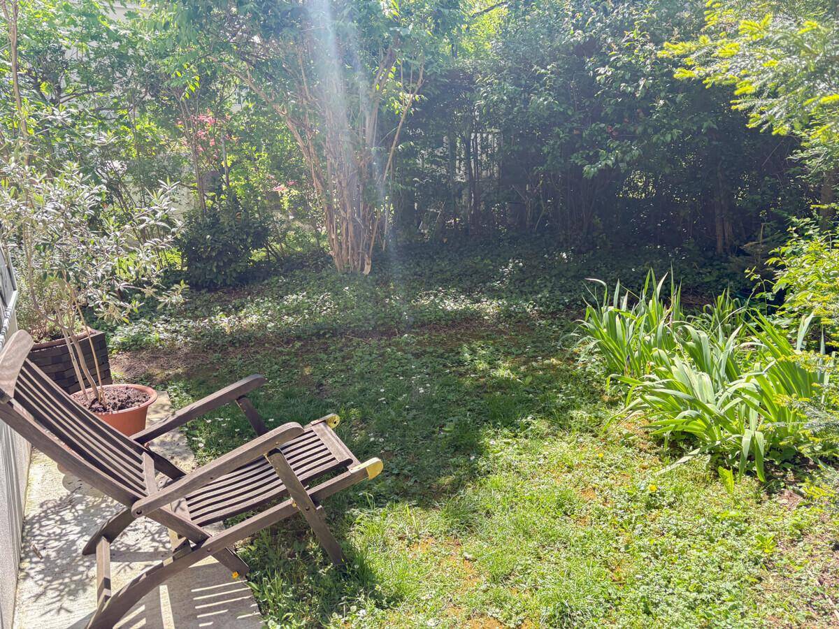 Sonniger Gartenbereich mit Rasenfläche, Pflanzen und zwei Holzliegestühlen zum Entspannen.