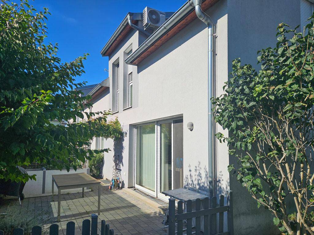 Seitenansicht des Hauses mit gepflasterter Terrasse und sichtbarer Klimaanlage.
