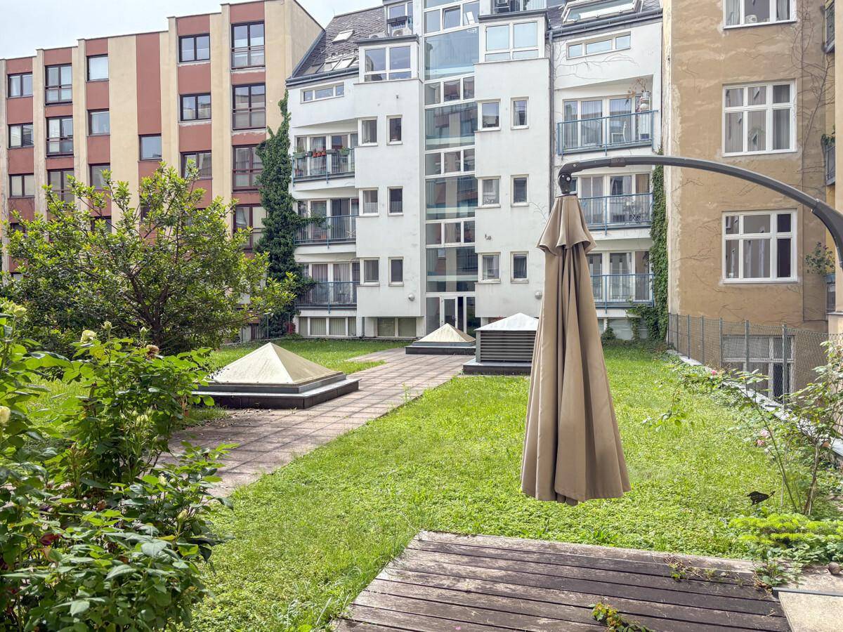 Begrünter Innenhof mit Rasenflächen, einem Holzdeck und einem Sonnenschirm, umgeben von modernen Gebäuden.