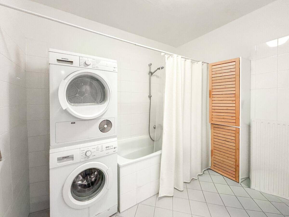 Badezimmer mit Badewanne, Duschvorhang und gestapelter Waschmaschine und Trockner.