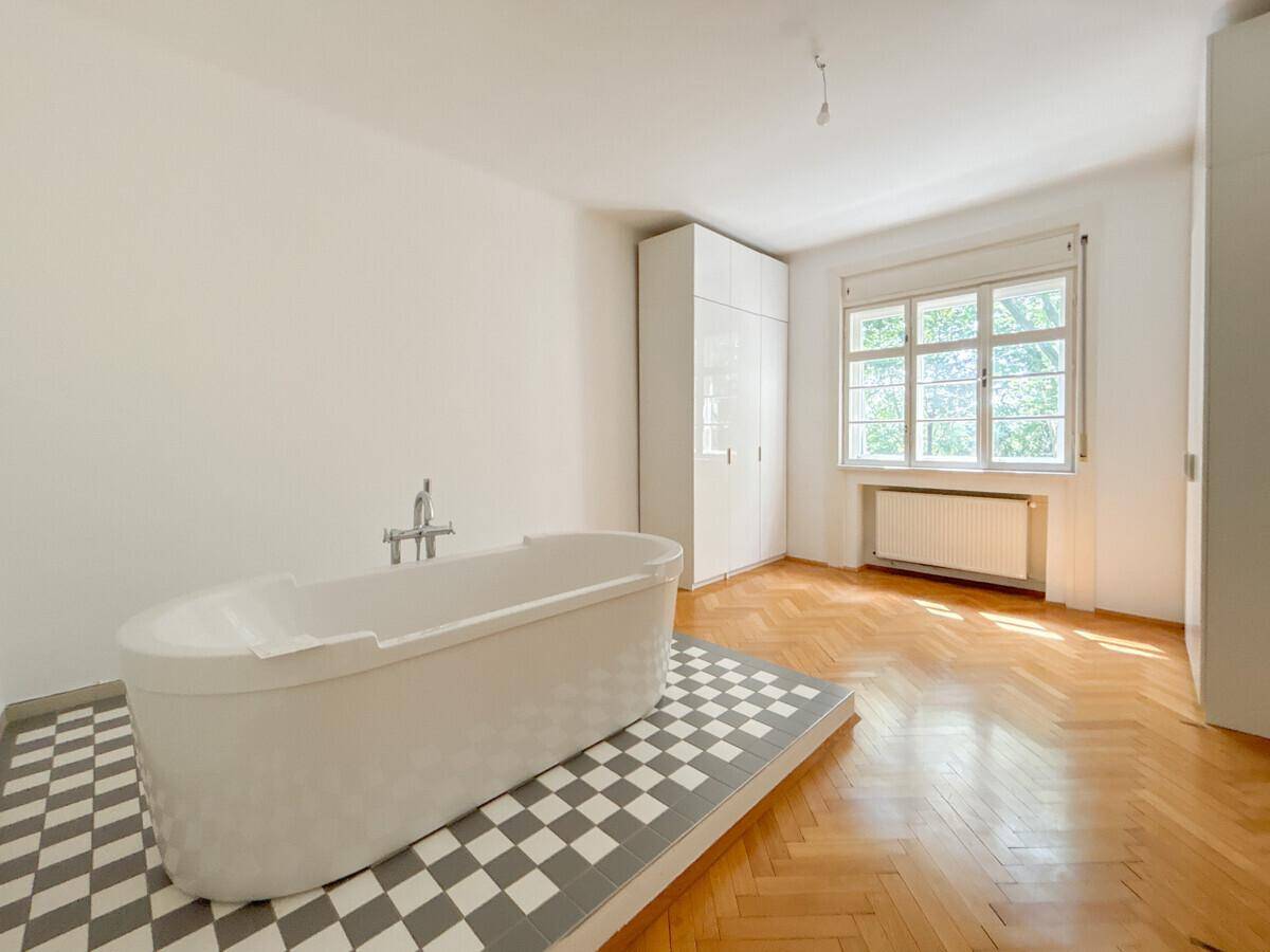 Großes Badezimmer mit freistehender Badewanne auf Podest und Fischgrätparkett.
