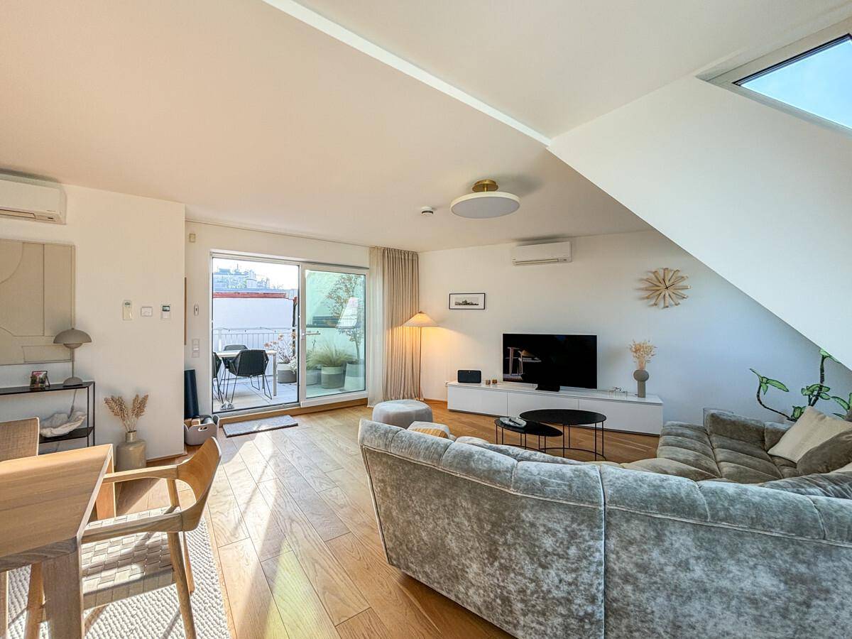 Helles Wohnzimmer mit Holzboden, modernem Sofa und direktem Zugang zur sonnigen Dachterrasse.