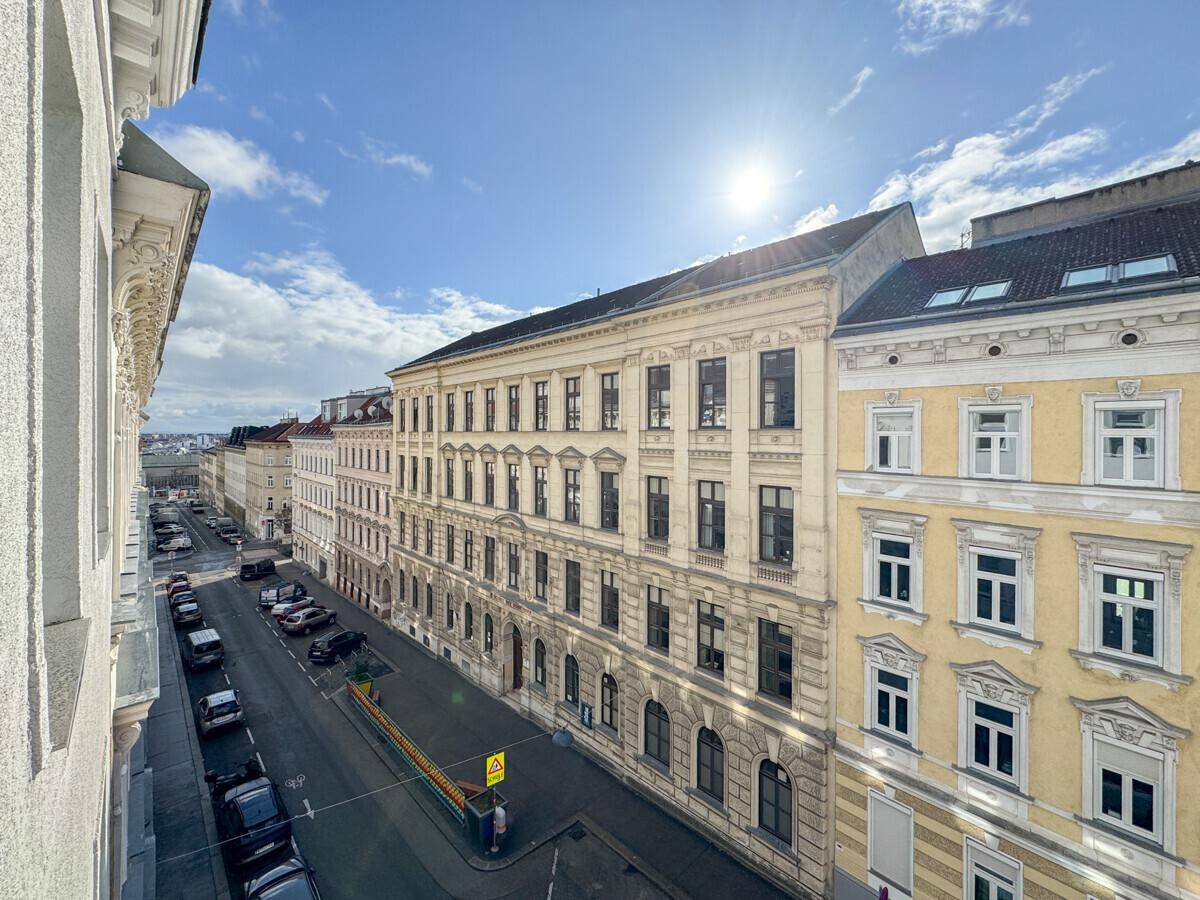 Blick von oben auf eine belebte Stadtstraße mit historischen Gebäuden unter blauem Himmel.