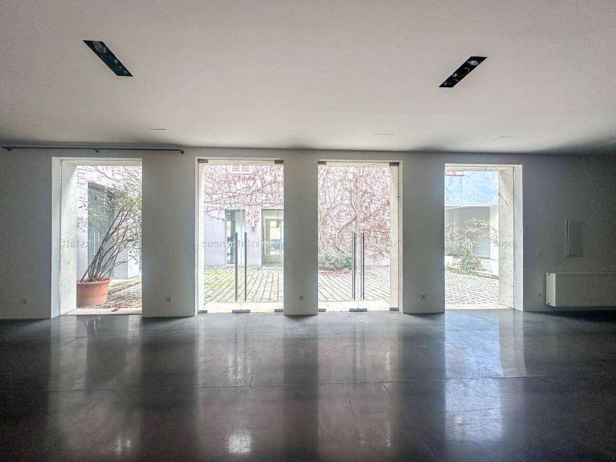 Heller, offener Raum mit Betonboden und mehreren großen Glastüren, die zu einem gepflasterten Innenhof führen.
