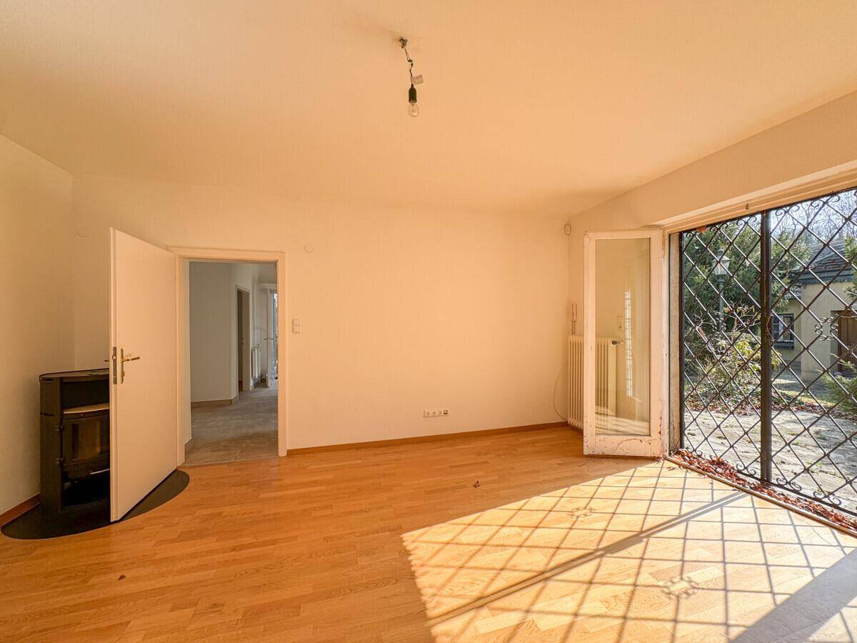 Geräumiges Wohnzimmer mit Holzboden, Kaminofen und Zugang zum Garten durch eine große Glastür.