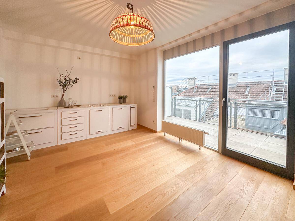 Heller Raum mit großen Fenstern, Holzboden und direktem Zugang zu einer Dachterrasse.