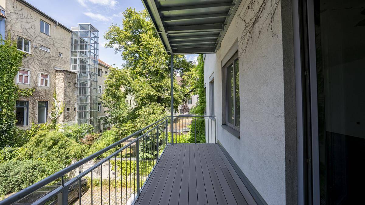 Balkon mit Holzboden und Blick auf den grünen Innenhof und den externen Glasaufzug.