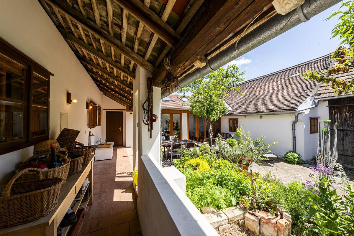 Überdachter Gang mit Terrakottaboden und Blick auf den grünen Innenhof, ideal als geschützter Außenbereich.