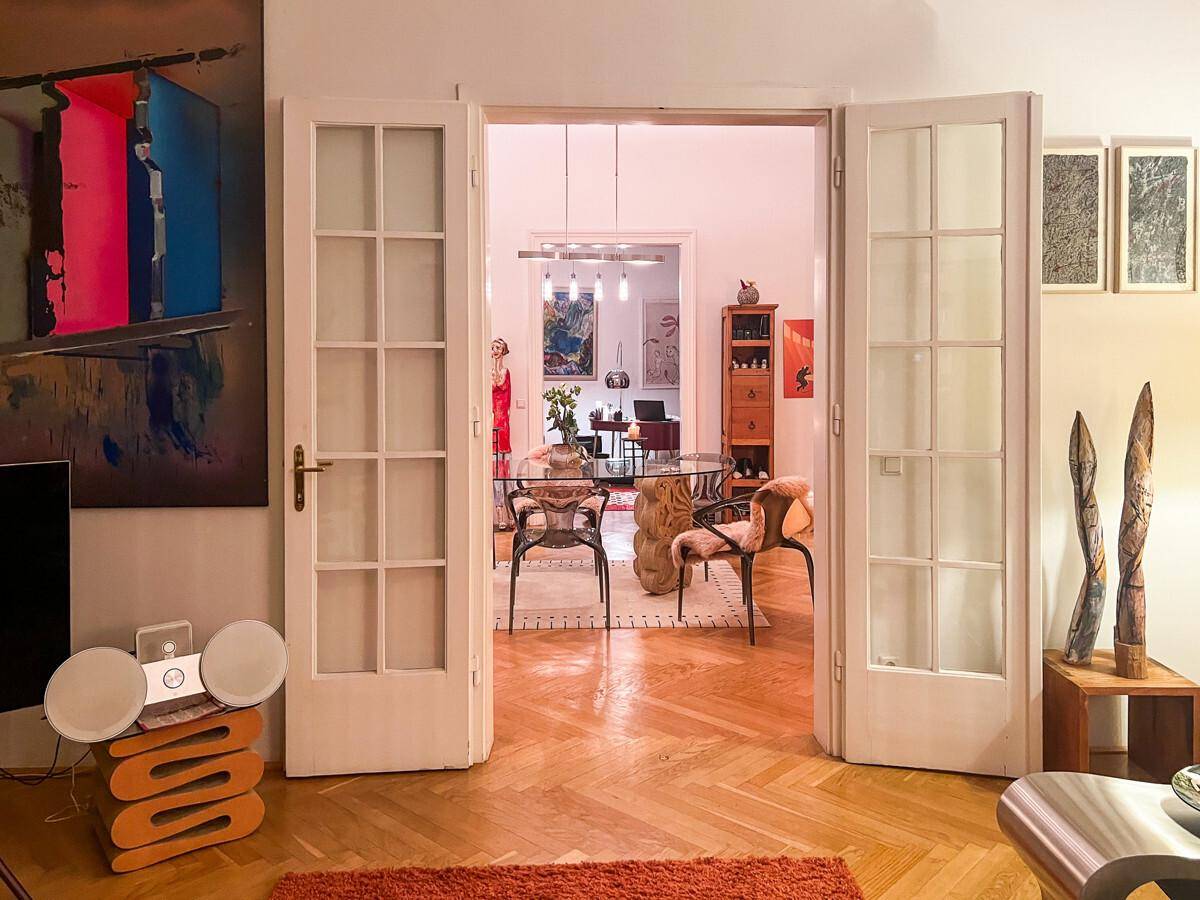 Helles Wohnzimmer mit Fischgrätparkett und Blick durch Flügeltüren in den Essbereich.