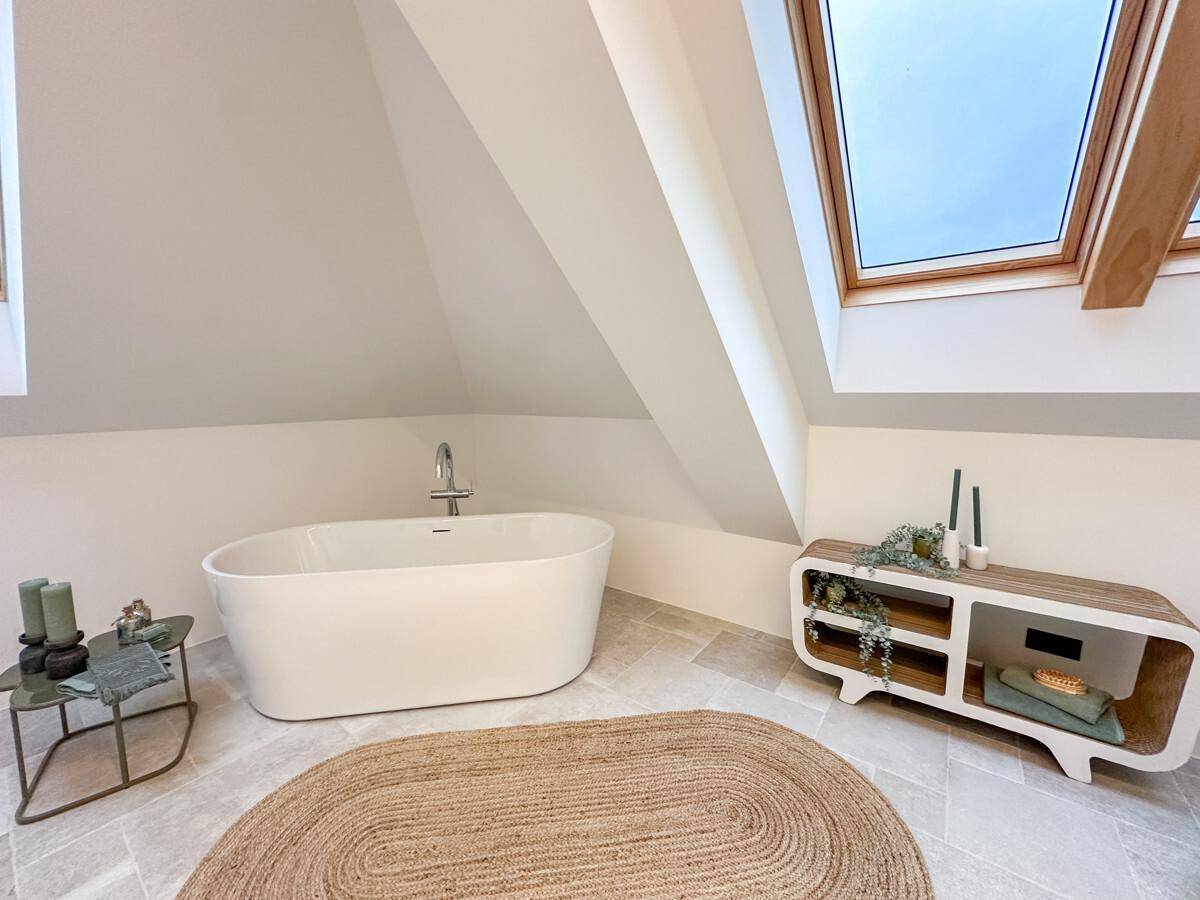 Geräumiges Badezimmer mit einer stilvollen freistehenden Badewanne unter einem Dachfenster und Fliesenboden.