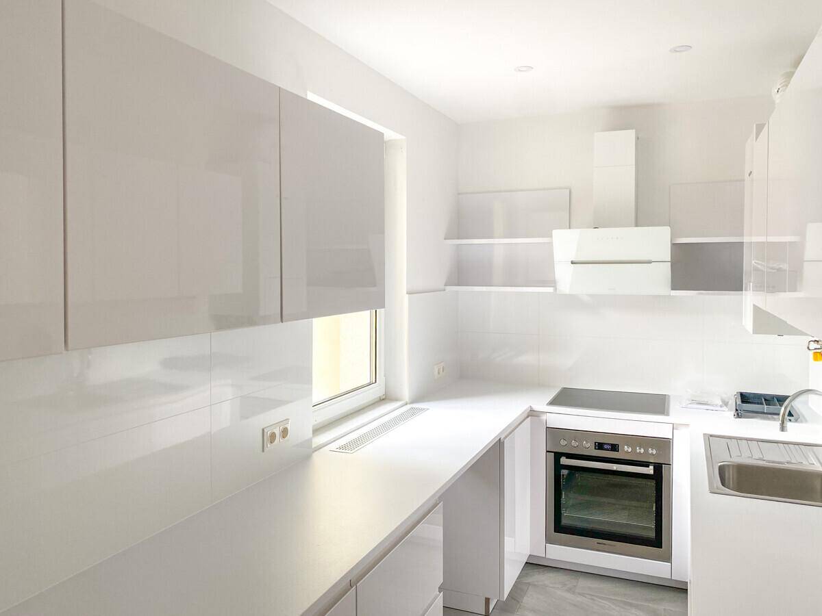 Moderne, helle Küche mit weißen Hochglanzfronten, integrierten Geräten und Fenster für Tageslicht.