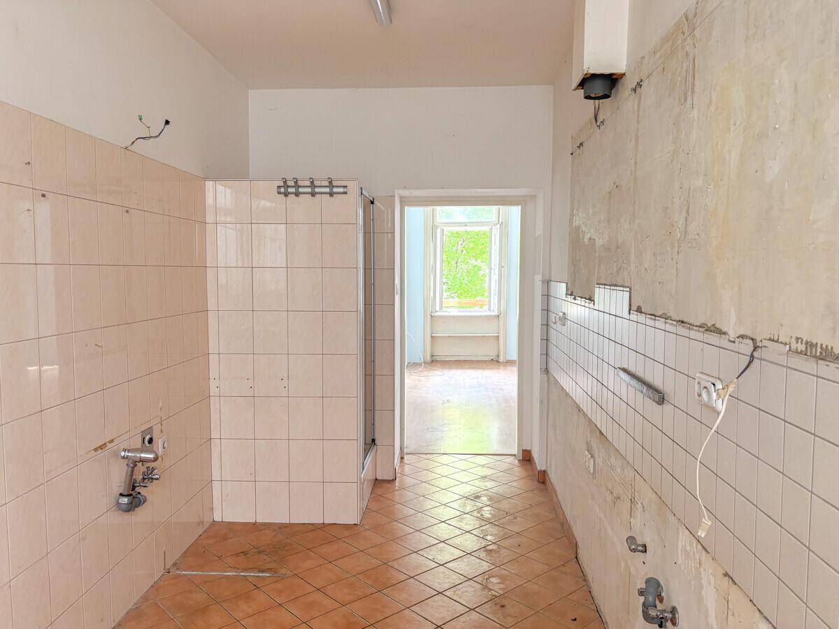 Badezimmer in Renovierung mit teilweise gefliesten Wänden, sichtbaren Leitungen und einer Duschkabine.