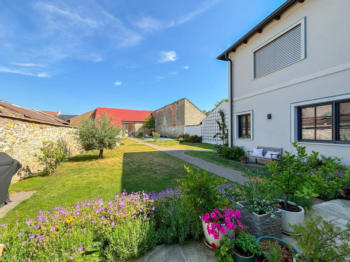 Sonniger Gartenbereich mit blühenden Blumenbeeten, Rasenfläche und Blick auf das Wohnhaus.