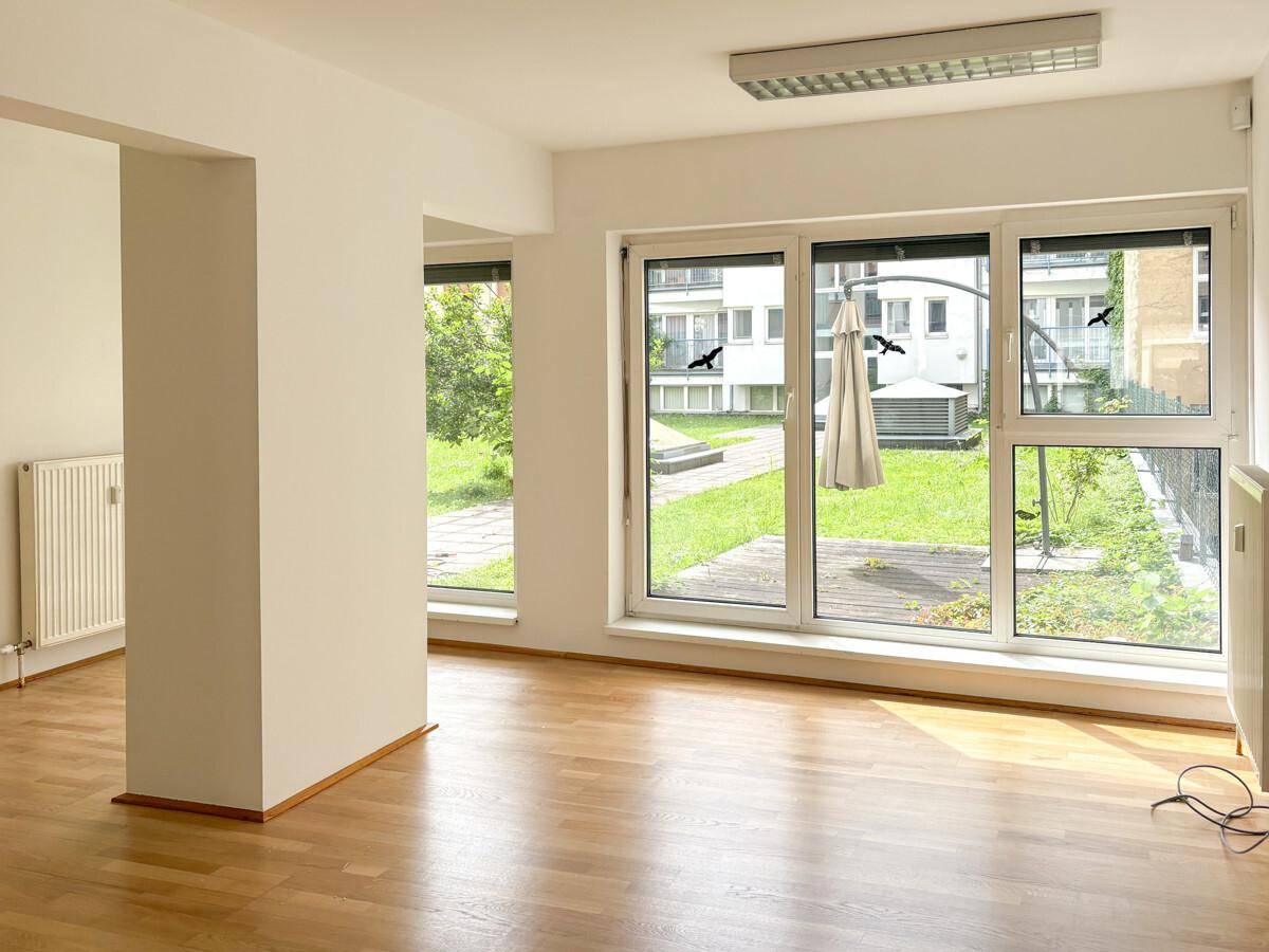 Geräumiger Innenraum mit großen Fenstern, die einen Blick auf den begrünten Innenhof und die umliegenden Gebäude bieten.