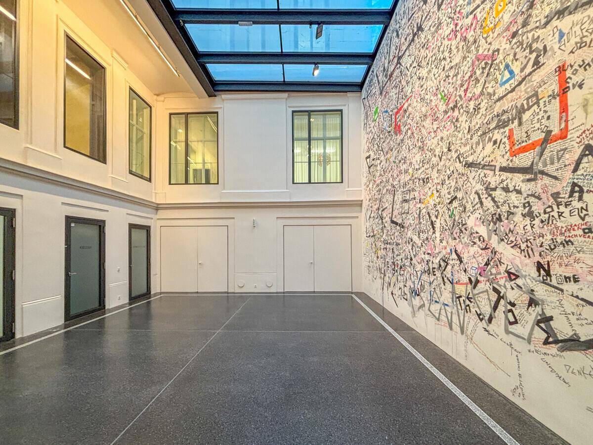 Großzügiges Atrium mit Glasdach, moderner Kunstwand und dunklem Boden, das viel Licht spendet.