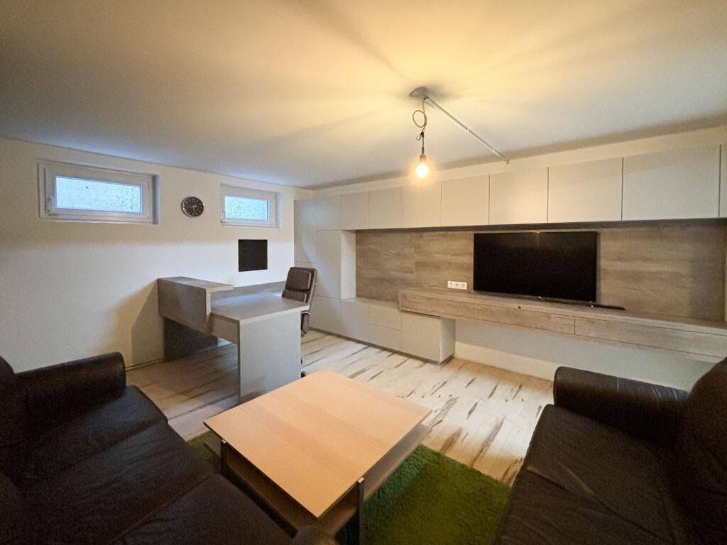 Helles Wohnzimmer mit integriertem Arbeitsbereich, TV-Möbel und hellem Laminatboden.