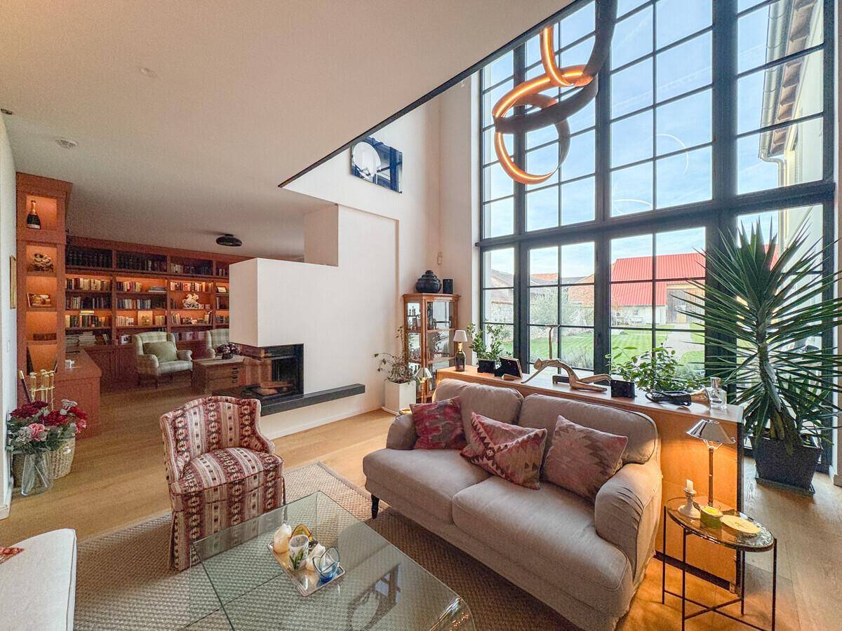 Geräumiges Wohnzimmer mit Kamin, hohen Decken und großen Fenstern, die viel Tageslicht hereinlassen.