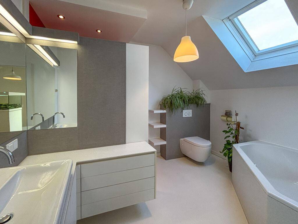 Helles Badezimmer mit Badewanne, wandhängendem WC, Doppelwaschbecken und Dachfenster.