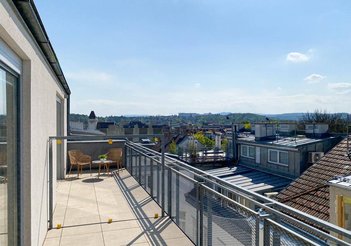 Sonniger Balkon mit Metallgeländer und Ausblick auf die umliegende Stadtlandschaft und Dächer.