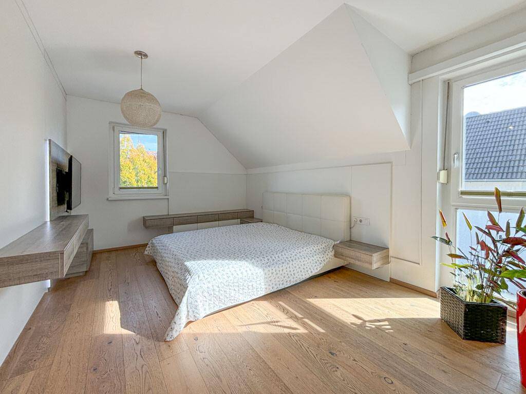 Helles Schlafzimmer im Dachgeschoss mit Holzboden, schrägen Decken und großen Fenstern.