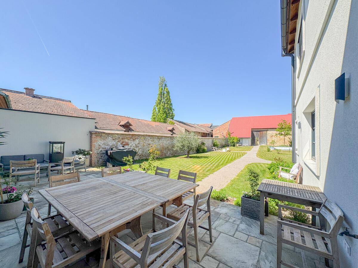 Große gepflasterte Terrasse mit Holztisch und Stühlen, ideal für Mahlzeiten im Freien und Entspannung.
