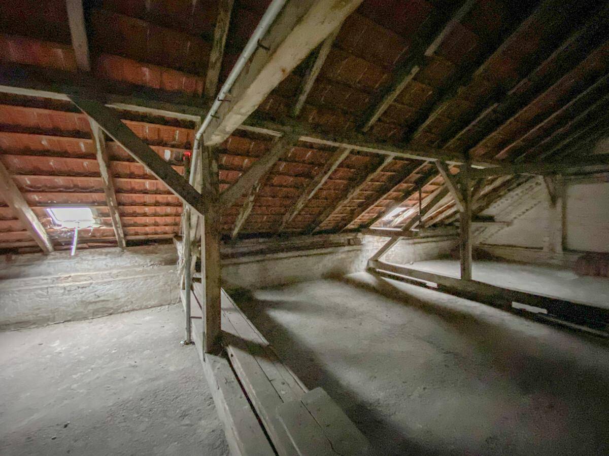 Unausgebauter Dachboden mit sichtbaren Holzbalken und Dachziegeln, bereit für den Ausbau.