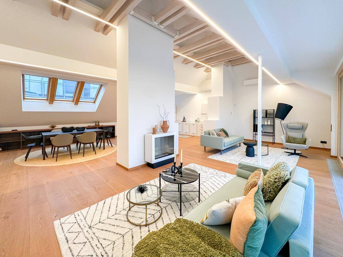 Geräumiger, offener Wohn- und Essbereich mit Holzboden, modernen Möbeln, Kamin und sichtbaren Dachbalken.