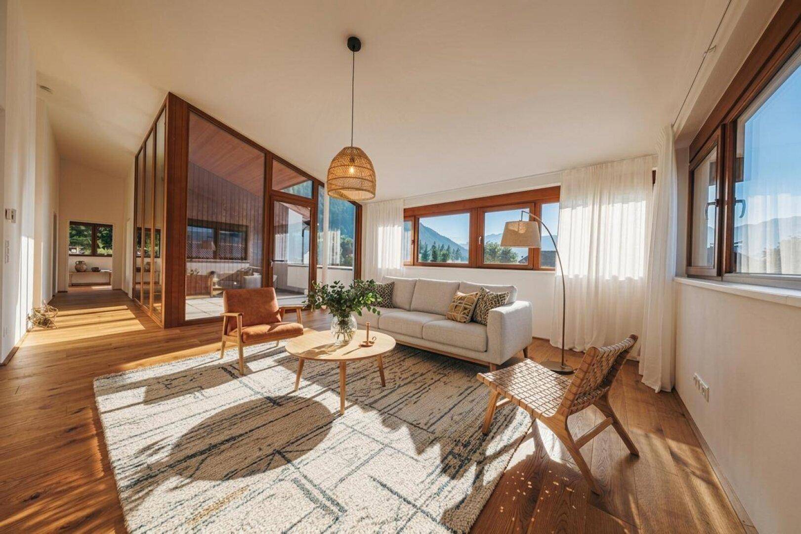 Helles Wohnzimmer mit Holzboden, gemütlicher Sitzecke und großen Fenstern mit Bergblick.