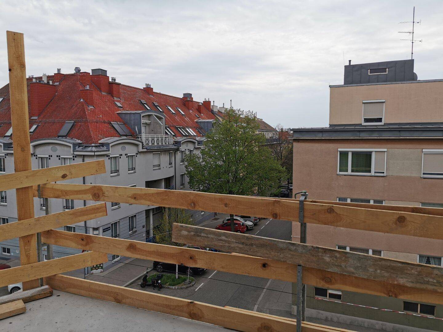 Blick von einem Gebäude im Bau auf die umliegende Wohngegend mit roten Dächern und einer Straße.