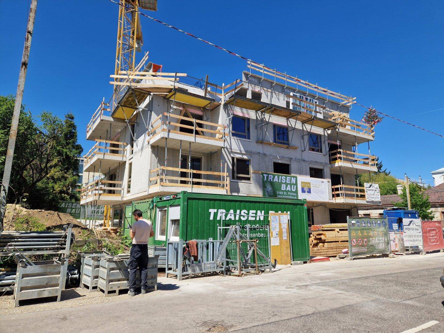 Fortschritt der Bauarbeiten an einem modernen Wohnhaus mit Kran und Baucontainern.